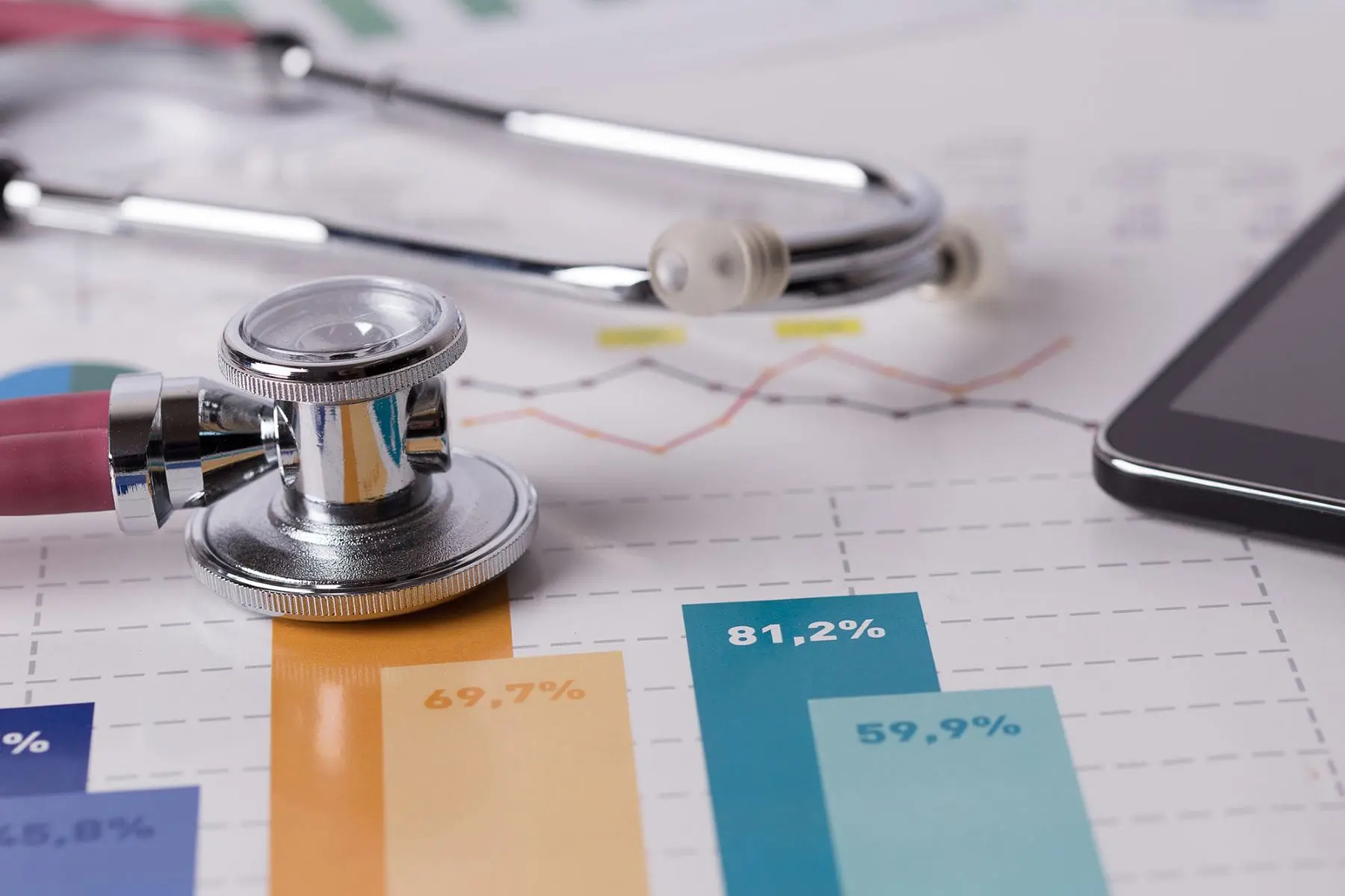 A stethoscope lies on a graph paper with printed data next to a syringe and a digital tablet.