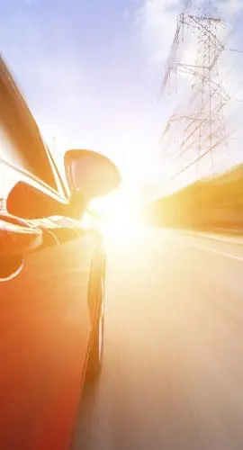 A red car is speeding down a road with motion blur effect suggesting high speed, under a sunny sky.