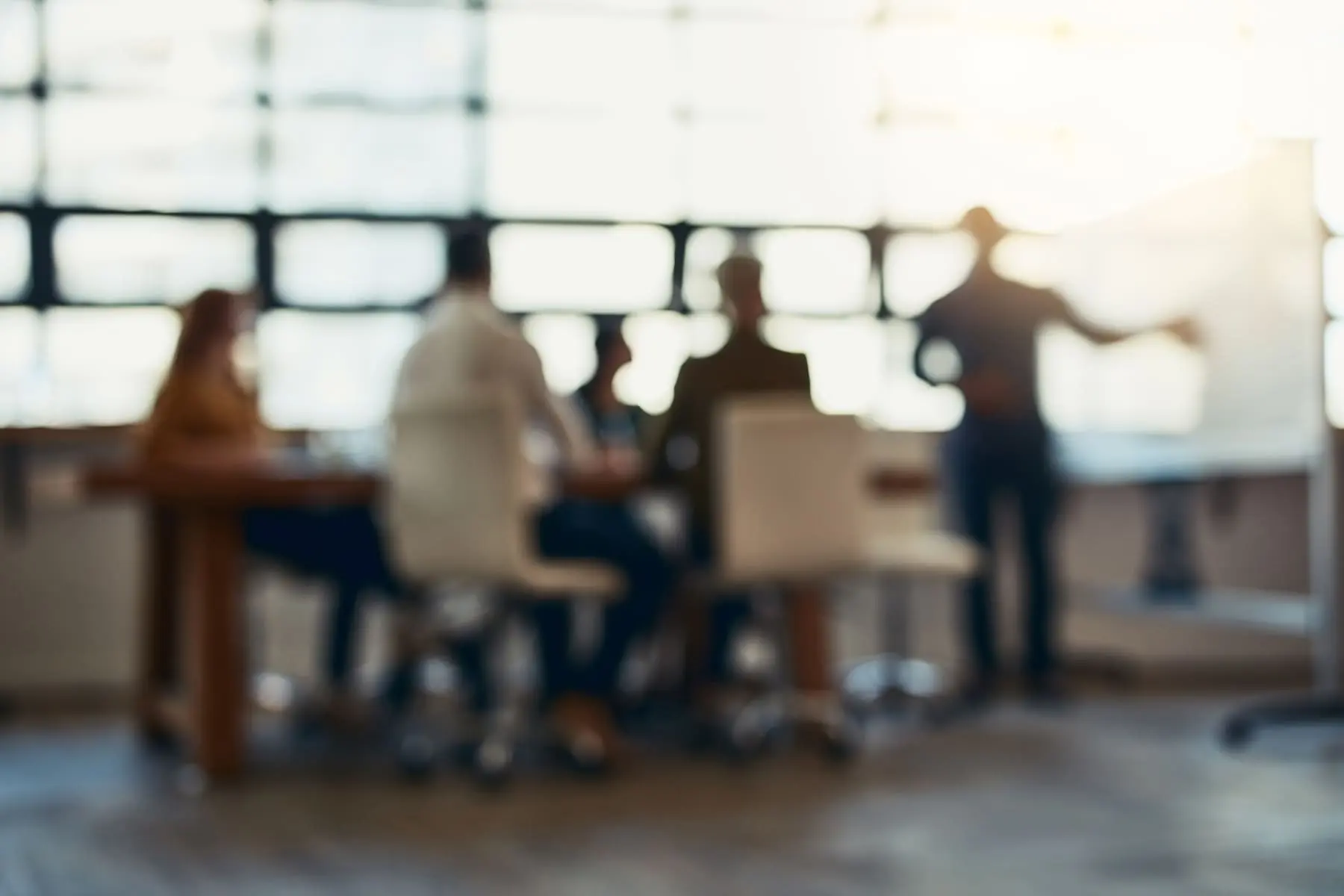 A group of individuals is engaged in various activities in a room with large windows during the day, with the scene out of focus.