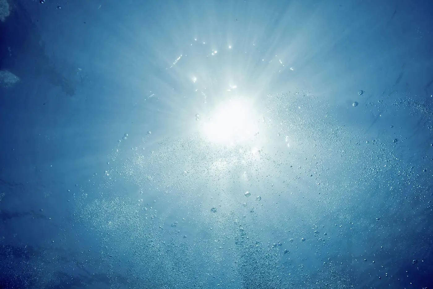 Sunlight filters through water, creating a pattern of light rays and bubbles.