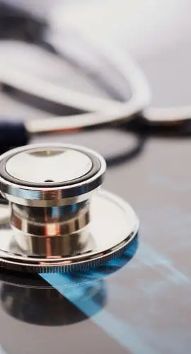 A stethoscope lies atop a reflective surface with an X-ray film beneath it.