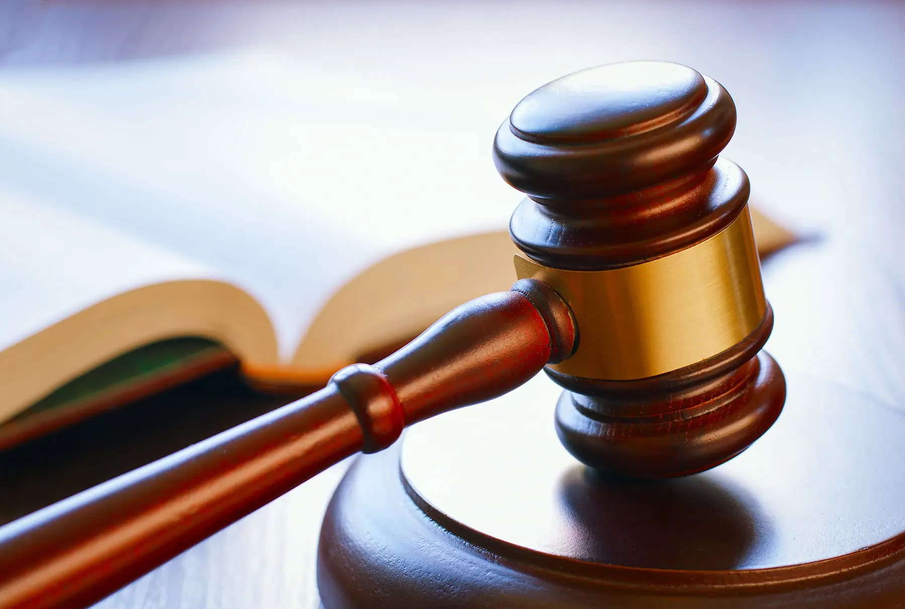 A wooden judge's gavel rests on a sounding block with a blurred legal book in the background.