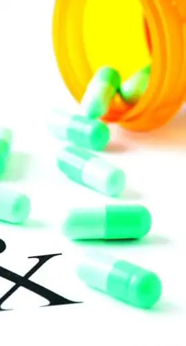 A spilled bottle of green capsules next to a prescription label with the symbol "Rx" visible.