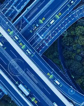 An aerial view of a complex highway interchange with multiple layers of roads and vehicles next to a forested area.