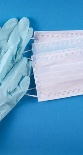 Blue medical gloves and white face masks are arranged on a blue surface.