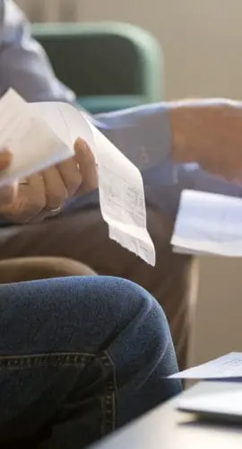 Two individuals are reviewing papers and receipts, with a calculator and a laptop nearby.