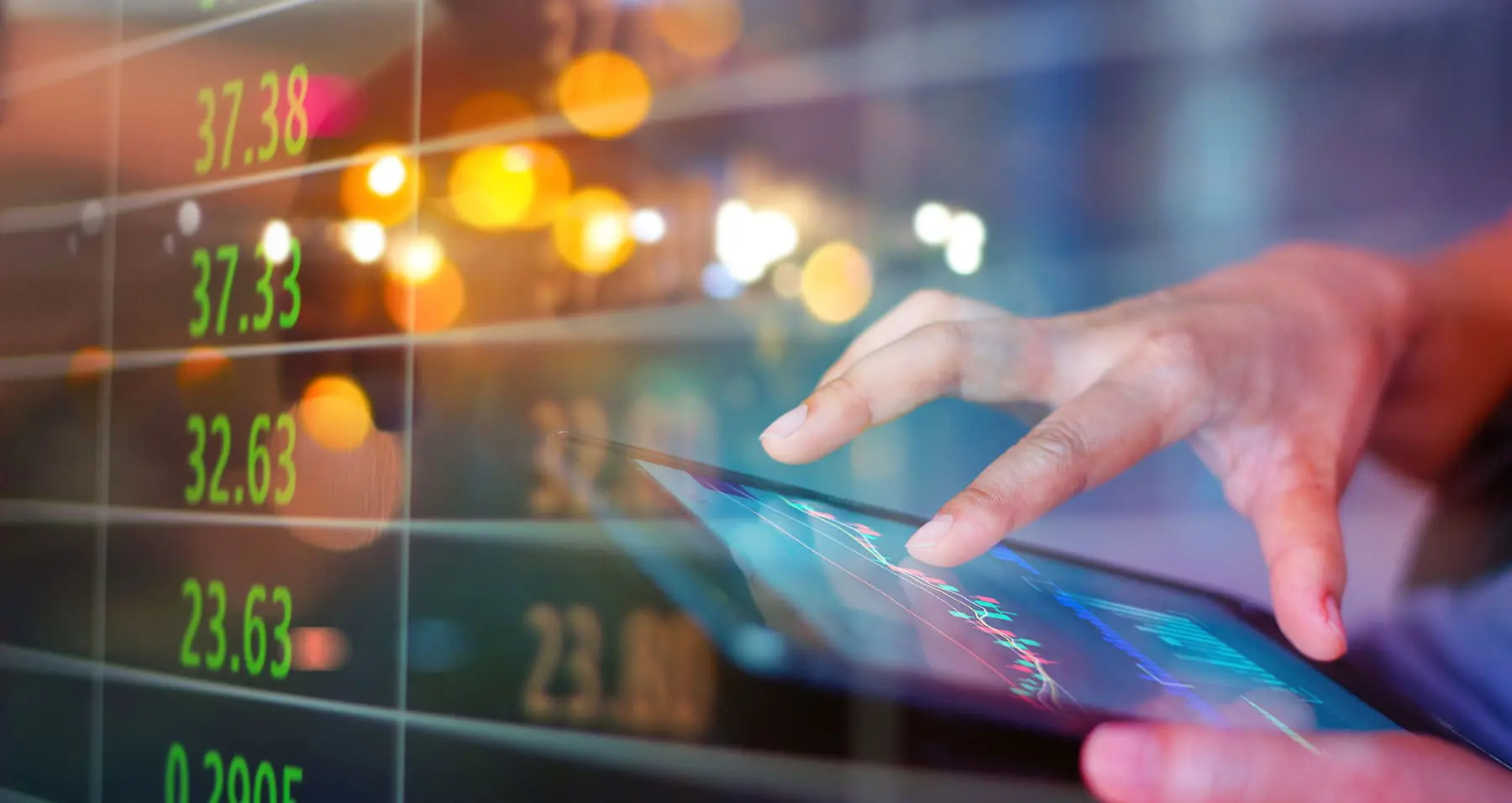 Hands operating a tablet with a digital stock market chart overlay displaying numerical data in the background.