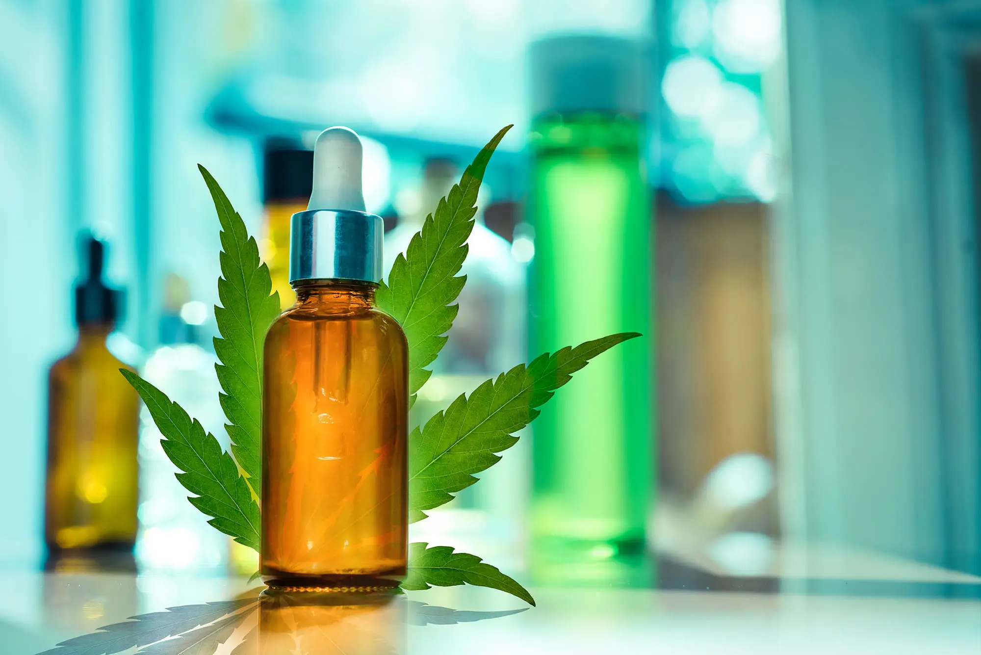A dropper bottle is placed in front of a cannabis leaf, with more bottles in the background.