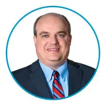 A person in a suit and tie is smiling, framed by a blue circle border.
