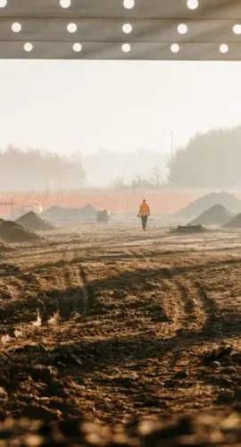 An industrial construction site under a large, unfinished structure with mounds of soil and metal framework.