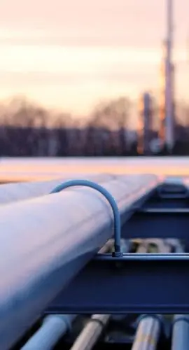 Industrial pipelines extending toward an oil refinery at dusk, representing produced water recycling infrastructure and oilfield wastewater transport in energy production.