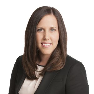A professional portrait of a woman with long brown hair, smiling, wearing a black blazer and a cream blouse.
