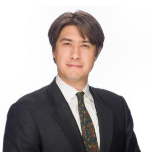 A man in a suit and tie poses against a plain white background.